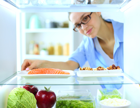 Portrait of female standing near open fridge full of healthy food, vegetables and fruits. Portrait of femaleの写真素材