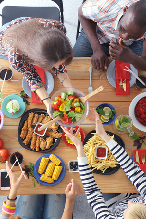 Top view of group of people having dinner together while sitting at wooden table. Food on the table. People eat fast food.の写真素材