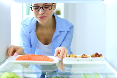 Portrait of female standing near open fridge full of healthy food, vegetables and fruits. Portrait of femaleの写真素材