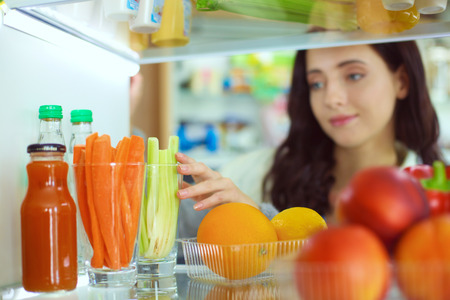 Portrait of female standing near open fridge full of healthy food, vegetables and fruits. Portrait of femaleの写真素材