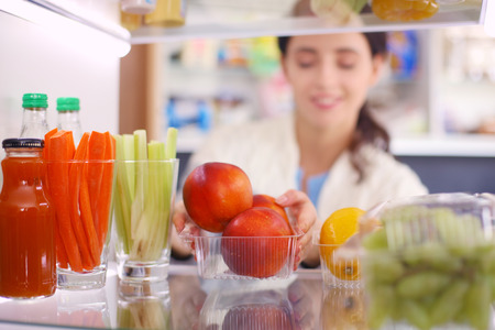 Portrait of female standing near open fridge full of healthy food, vegetables and fruits. Portrait of femaleの写真素材