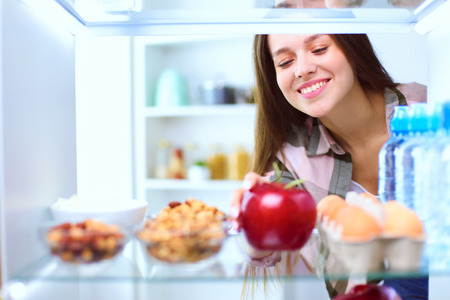 Portrait of female standing near open fridge full of healthy food, vegetables and fruits. Portrait of femaleの写真素材