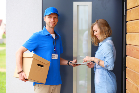 Smiling delivery man in blue uniform delivering parcel box to recipient - courier service concept. Smiling delivery man in blue uniformの写真素材