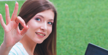 Young woman with laptop sitting on green grass . Portreit young womanの写真素材