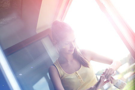 Woman painting wall of an apartment with a paintbrush carefully finishing off around window frameの写真素材