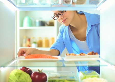 Portrait of female standing near open fridge full of healthy food, vegetables and fruits.の写真素材