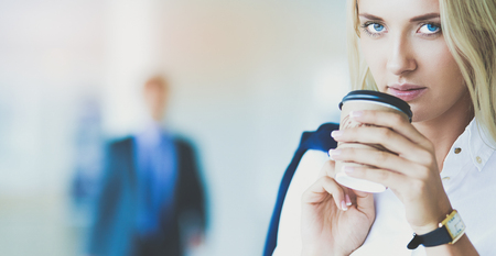Businesswoman standing against office window talking on mobile phoneの写真素材