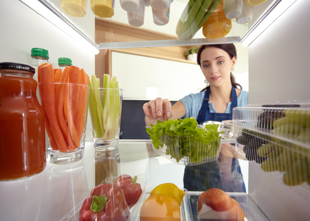 Portrait of female standing near open fridge full of healthy food, vegetables and fruits. Portrait of femaleの写真素材