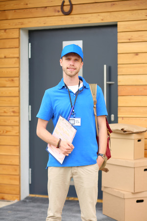 Smiling delivery man in blue uniform delivering parcel box to recipient - courier service concept. Smiling delivery man in blue uniformの写真素材