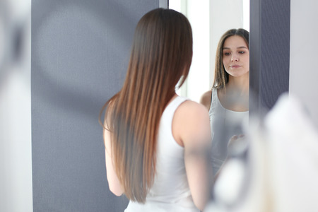Young woman looking herself reflection in mirror at home.の写真素材