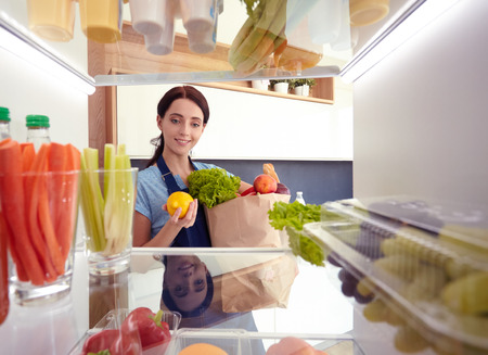 Portrait of female standing near open fridge full of healthy food, vegetables and fruits. Portrait of femaleの写真素材