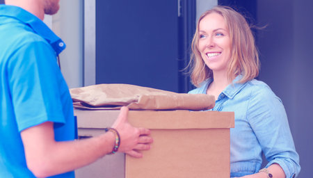 Smiling delivery man in blue uniform delivering parcel box to recipient - courier service concept....