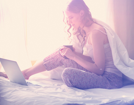 Young beautiful woman sitting in bed with laptop.の写真素材