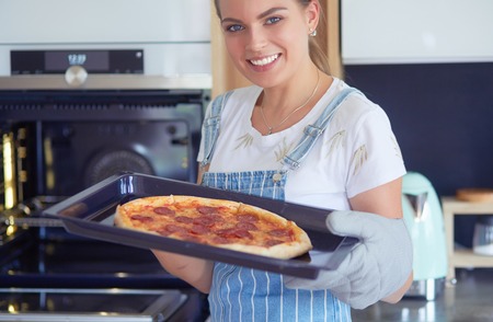 Happy young woman cooking pizza at homeの写真素材
