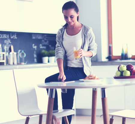 Young woman with orange juice and tablet in kitchenの写真素材