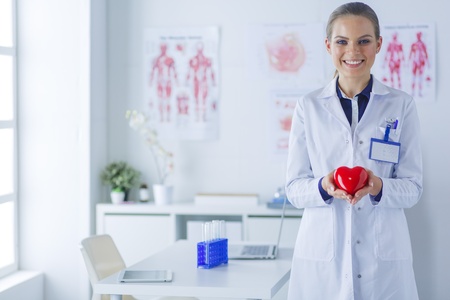 A doctor with stethoscope examining red heart, isolated on white backgroundの写真素材
