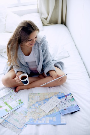 Relaxed young woman sitting on bed with a cup of coffee and digital tabletの写真素材
