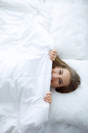 Face closeup of a beautiful young woman hiding her face under the sheetの写真素材