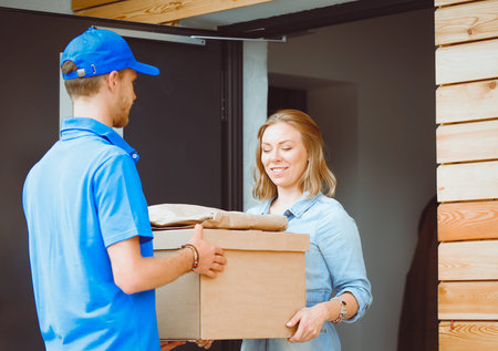 Smiling delivery man in blue uniform delivering parcel box to recipient - courier service concept....
