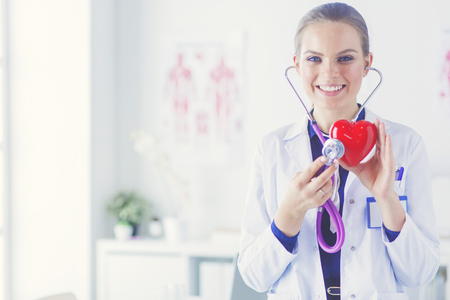 A doctor with stethoscope examining red heart, isolated on white backgroundの写真素材