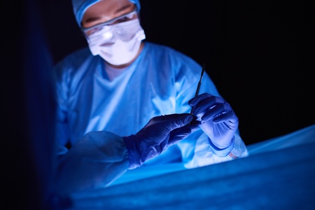Doctor performing surgery in a dark background.の写真素材