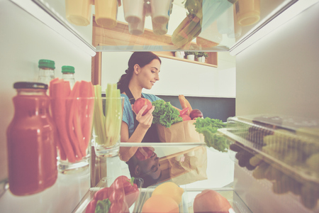Portrait of female standing near open fridge full of healthy food, vegetables and fruits.の写真素材