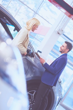 Dealer with woman stands near a new car in the showroomの写真素材