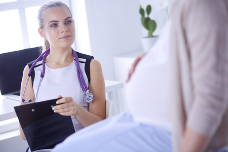 Young woman doctor with stethoscope and tablet speaking with pregnant woman at hospital.の写真素材