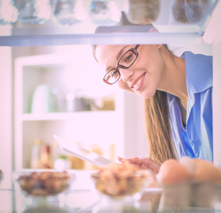 Portrait of female standing near open fridge full of healthy food, vegetables and fruits. Portrait of femaleの写真素材