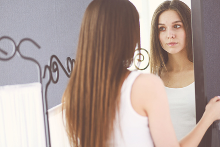Young woman looking herself reflection in mirror at home.の写真素材