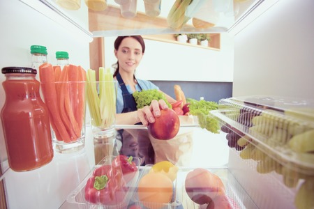 Portrait of female standing near open fridge full of healthy food, vegetables and fruits.の写真素材