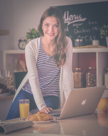 Attractive young woman using laptop and sitting in the kitchenの写真素材