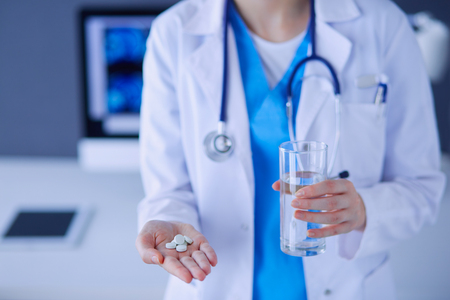 Close-up shot of doctor's hands holding pills and glass of waterの写真素材