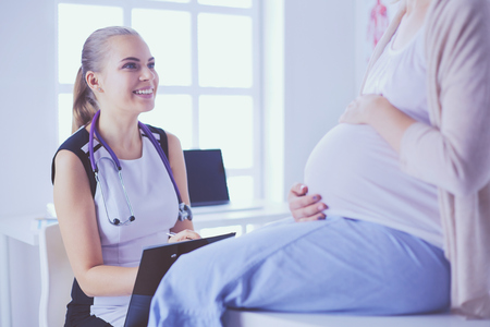 Young woman doctor with stethoscope and tablet speaking with pregnant woman at hospital.の写真素材