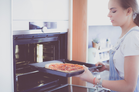 Happy young woman cooking pizza at homeの写真素材