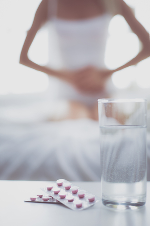 Young beautiful woman with pills lying on bed in bedroomの写真素材