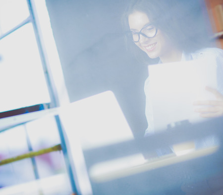 Young woman sitting at office table with laptop,view through window. Young womanの写真素材