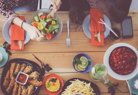 Top view of group of people having dinner together while sitting at wooden table. Food on the table. People eat fast food.の写真素材