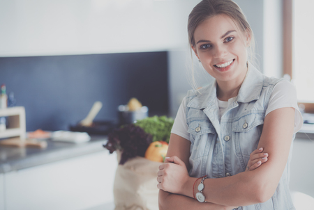 Portrait of young woman standing with arms crossed against kitchen backgroundの写真素材