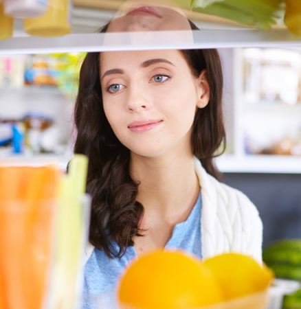 Portrait of female standing near open fridge full of healthy food, vegetables and fruits.の写真素材