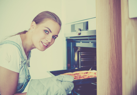 Happy young woman cooking pizza at homeの写真素材