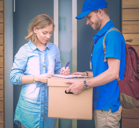 Smiling delivery man in blue uniform delivering parcel box to recipient - courier service concept.の写真素材