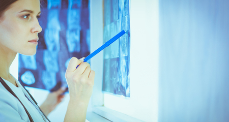 Young smiling female doctor with stethoscope pointing at X-ray at doctors officeの写真素材