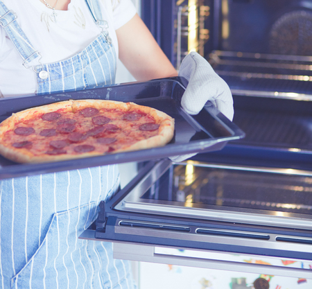 Happy young woman cooking pizza at homeの写真素材