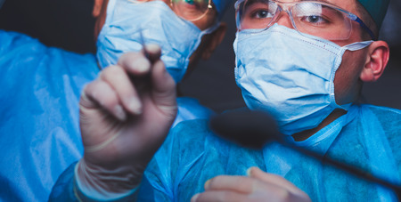 Group of surgeons at work in operating theater toned in blue. Medical team performing operationの写真素材