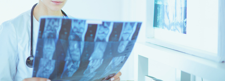 Young smiling female doctor with stethoscope looking at X-ray at doctors officeの写真素材