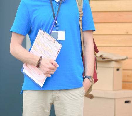Smiling delivery man in blue uniform delivering parcel box to recipient - courier service conceptの写真素材