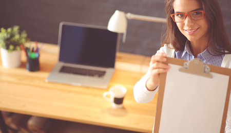 Young woman standing near desk with laptop holding folder and cup of coffee. Workplace. Business Woman.の写真素材