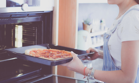 Happy young woman cooking pizza at homeの写真素材