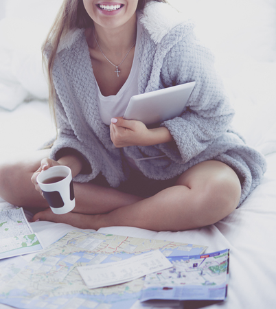 Relaxed young woman sitting on bed with a cup of coffee and digital tabletの写真素材
